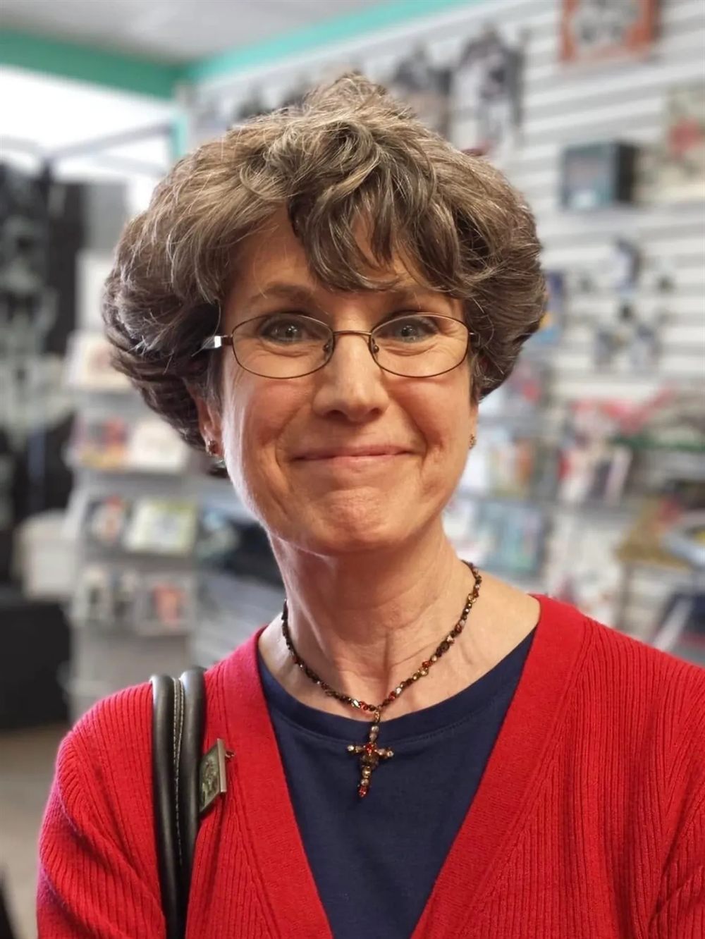 Pat Tarantino smiling, wearing a red cardigan and a beaded cross necklace